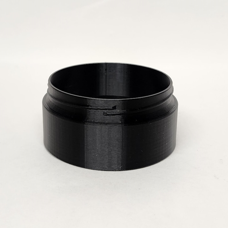 May include: A black, cylindrical container with a wide opening and a slightly raised rim. The container has a smooth, matte finish and appears to be made of plastic. The design is simple and functional, suitable for storing small items.
