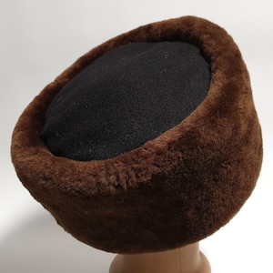 May include: A brown faux fur hat with a black felt top. The hat is designed with a wide brim and a soft, plush texture.