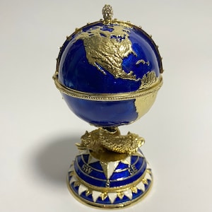 May include: A blue and gold globe with a compass rose on the base. The globe is decorated with gold continents and a gold fish on the base.