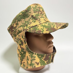 Puede incluir: Un sombrero de camuflaje con visera y cubrecuello. El sombrero presenta un patrón de camuflaje digital en tonos verdes, marrones y amarillos. El sombrero está diseñado para proteger del sol y los elementos.