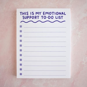 May include: A white notepad with the text "THIS IS MY EMOTIONAL SUPPORT TO-DO LIST" in purple. The notepad has a wavy line design and a series of purple boxes for checkmarks. The notepad is lined and ready to be filled out.