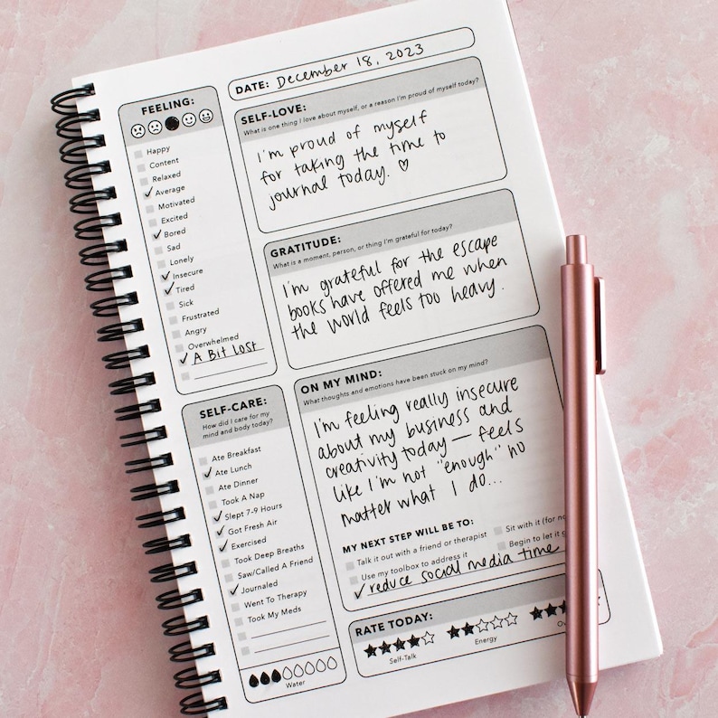 a spiral-bound notebook with a pen resting on top of it, displaying a self-care journal page with prompts for reflection and self-care activities.