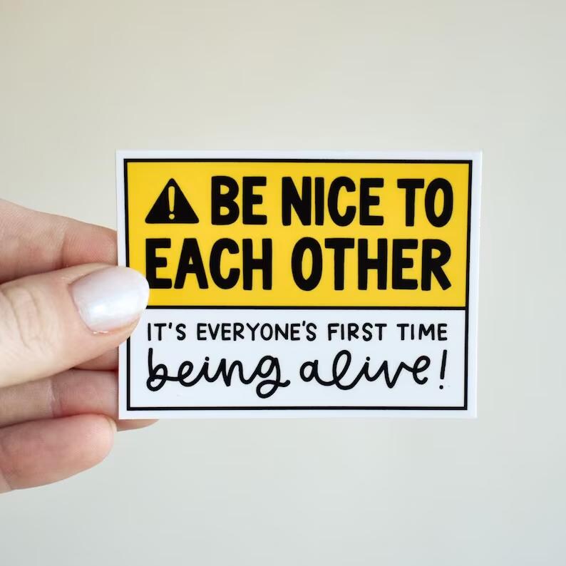 May include: A rectangular sticker with a yellow top section featuring a black warning triangle icon and the text BE NICE TO EACH OTHER. The white bottom section contains the black text IT'S EVERYONE'S FIRST TIME being alive! in a mix of fonts.