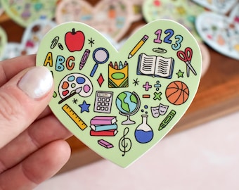 May include: A heart-shaped sticker with a light green background featuring colorful school-themed illustrations including an apple, ABC letters, a magnifying glass, a crayon box, a globe, a calculator, a basketball, a book, and math symbols.