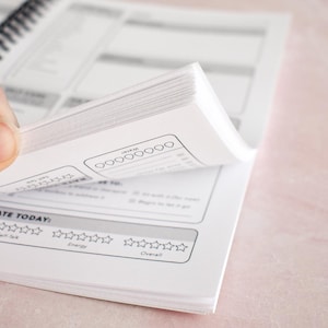 a hand holding open a notebook or book with a page that appears to be a survey or feedback form. The form has multiple sections, including a section for rating the form and another section for rating the user's experience. The form also includes a section for rating the user's energy levels.