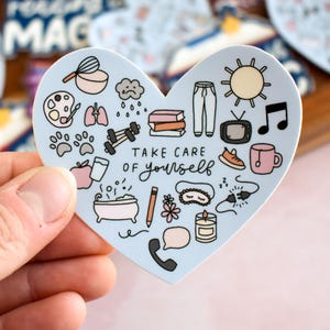 May include: A heart-shaped sticker with a light blue background featuring various small illustrations including a sun, books, a bathtub, a candle, and a telephone. The text "TAKE CARE OF yourself" is printed in the center in black ink.