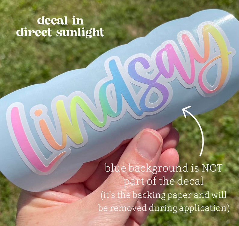 May include: A decal with the name "Lindsay" in a rainbow gradient font. The decal is shown on a light blue surface. Text in the image reads "decal in direct sunlight" and "blue background is NOT part of the decal (it's the backing paper and will be removed during application)".