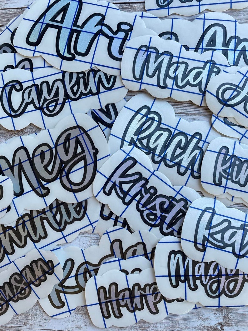 May include: A collection of white, cloud-shaped vinyl stickers with various names in a cursive font. The names are in a gradient color scheme with a black outline. Each sticker has a blue grid pattern.