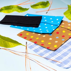 May include: Four fabric pouches in different patterns and colors. The pouches are stacked on top of each other. The top pouch is black, the second pouch is blue with white polka dots, the third pouch is brown with yellow and red flowers, and the bottom pouch is blue and white checkered.