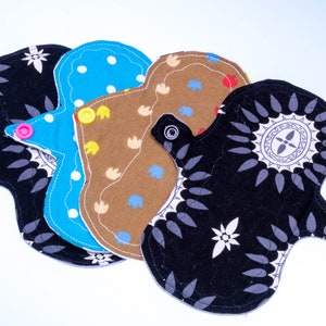 May include: Four reusable cloth menstrual pads in different colors and patterns. The pads are made of soft, absorbent fabric and have snaps for easy fastening.