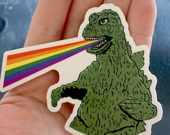 May include: A green monster with a rainbow coming out of its mouth. The monster is a cartoon illustration of Godzilla.
