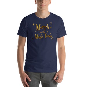 May include: A navy blue t-shirt with a gold graphic that reads "Murph and the Magic Tones" with musical notes and stars.