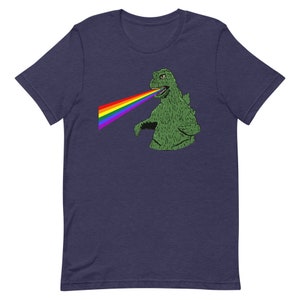 Puede incluir: Una camiseta azul marino con un monstruo verde disparando un arcoíris de su boca.