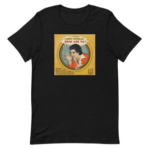 May include: A black t-shirt with a vintage record album design featuring Bobby Rydell. The album cover is yellow with a red and white image of Bobby Rydell. The album title is "How Are Ya?" and the album is by "Bobby Rydell".