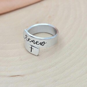 May include: A silver ring with the word "renew" and a cross engraved on it.