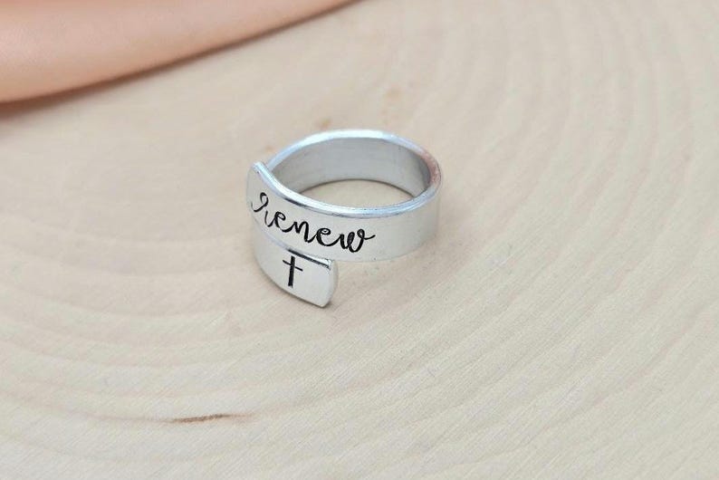 May include: A silver ring with the word "renew" and a cross engraved on it.
