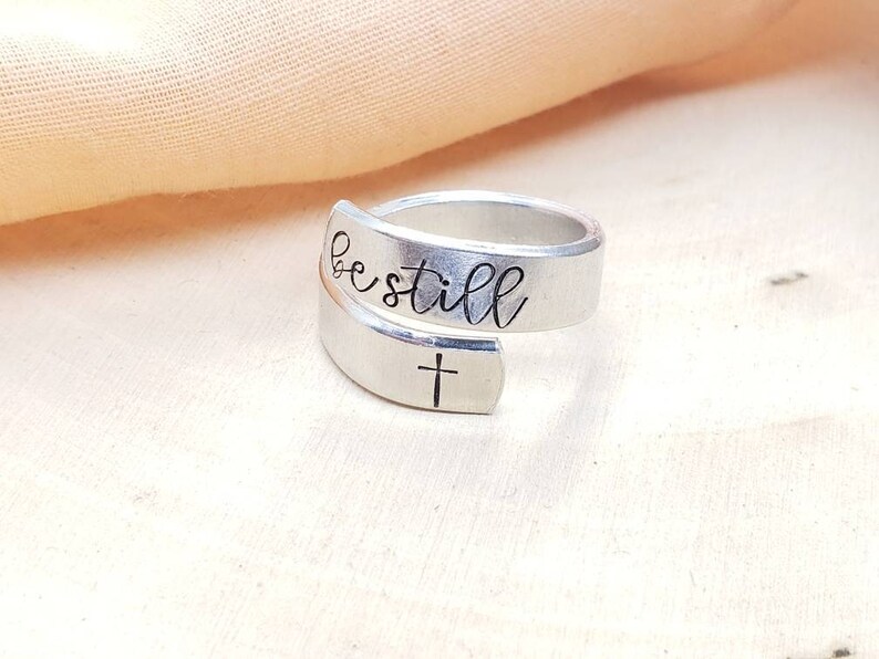 May include: A silver ring with the words "be still" engraved on it. A small cross is engraved on the band.