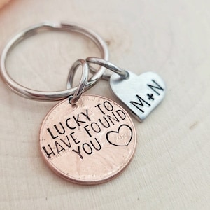 May include: A copper penny keychain with the text "Lucky to have found you" and a small heart. A silver heart charm with the text "M+N" is attached to the keychain.