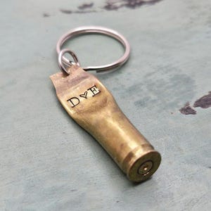 May include: A brass bullet casing keychain with a silver key ring. The casing is engraved with the initials "D & E" and a heart symbol.
