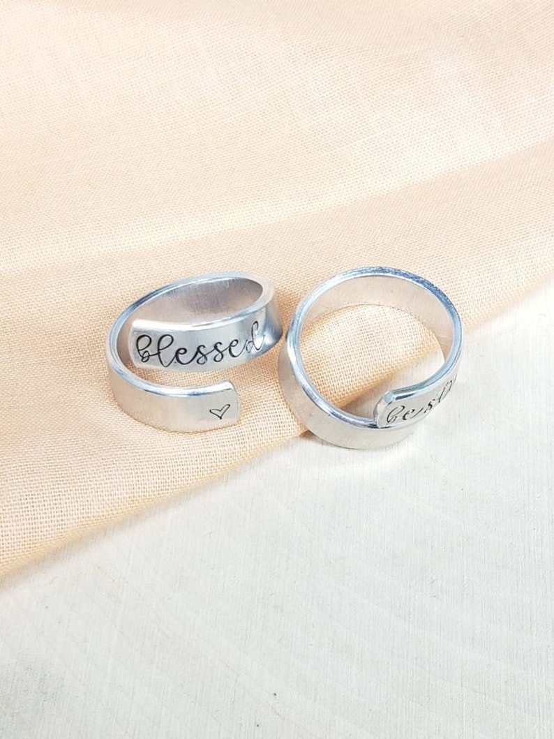 May include: Two silver rings with the words "blessed" and "beside" engraved on them. The ring with the word "blessed" also has a small heart engraved on it.