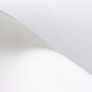 Pode incluir: Uma foto em close-up de um papel branco texturizado com uma ligeira curva. O papel tem uma superf&iacute;cie subtil e granulada contra um fundo branco brilhante, criando uma est&eacute;tica limpa e minimalista.
