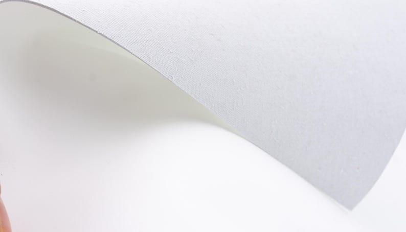 Pode incluir: Uma foto em close-up de um papel branco texturizado com uma ligeira curva. O papel tem uma superf&iacute;cie subtil e granulada contra um fundo branco brilhante, criando uma est&eacute;tica limpa e minimalista.
