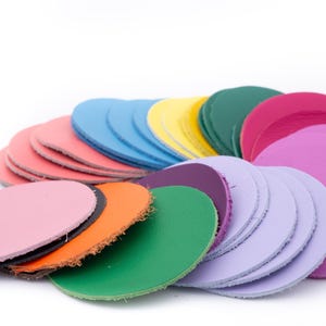 Può includere: Una collezione di pezzi di pelle rotondi e colorati in varie tonalità, tra cui rosa, arancione, verde, viola, blu e giallo. I cerchi di pelle sono impilati e disposti, mostrando i loro diversi colori e trame.