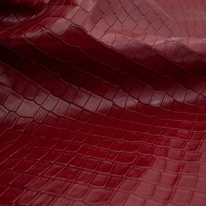 May include: Red faux leather with a crocodile embossed pattern. The leather is folded and textured.