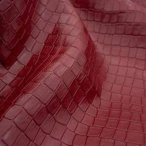 May include: Close-up of a deep red textured fabric with a crocodile skin pattern.
