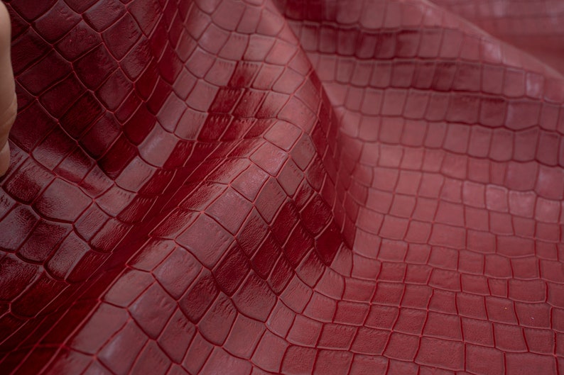 May include: Close-up of a deep red textured fabric with a crocodile skin pattern.