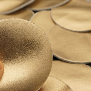 May include: A close-up of a gold leather circle with a textured surface. The circle is surrounded by other similar circles, creating a pattern.