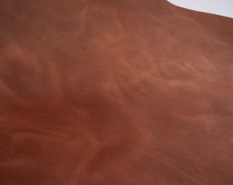Może przedstawiać: Zbliżenie na kawałek brązowej skóry. Skóra ma bogaty, ciepły kolor z odcieniami i teksturą. Powierzchnia wykazuje subtelne wzory i naturalne ślady.