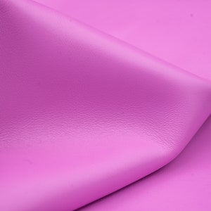 May include: A close-up of a smooth, soft, pink leather fabric. The fabric is folded in a way that shows its texture and color.