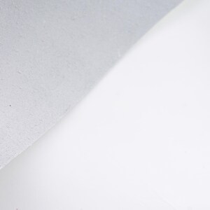 Pode incluir: Um close-up de uma superf&iacute;cie branca com um canto texturizado cinza claro. O canto &eacute; ligeiramente curvo, revelando um vislumbre do fundo branco. A imagem &eacute; bem iluminada, destacando o contraste das texturas.