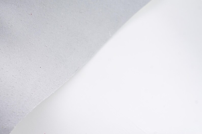 Pode incluir: Um close-up de uma superf&iacute;cie branca com um canto texturizado cinza claro. O canto &eacute; ligeiramente curvo, revelando um vislumbre do fundo branco. A imagem &eacute; bem iluminada, destacando o contraste das texturas.