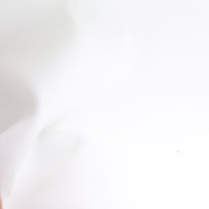 Pode incluir: Um close-up de tecido branco com dobras suaves. O tecido &eacute; liso e parece ser feito de um material leve. A imagem &eacute; bem iluminada, destacando a textura e o movimento do tecido.