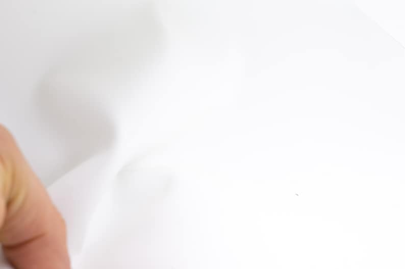 Pode incluir: Um close-up de tecido branco com dobras suaves. O tecido &eacute; liso e parece ser feito de um material leve. A imagem &eacute; bem iluminada, destacando a textura e o movimento do tecido.
