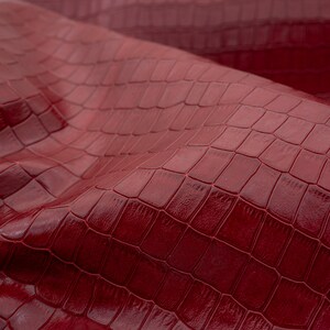 May include: Close-up of a burgundy faux leather fabric with a crocodile embossed pattern.