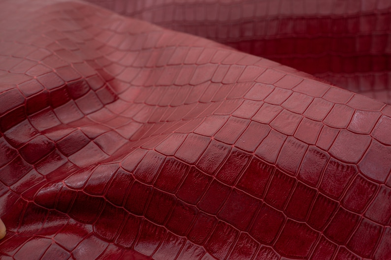 May include: Close-up of a burgundy faux leather fabric with a crocodile embossed pattern.