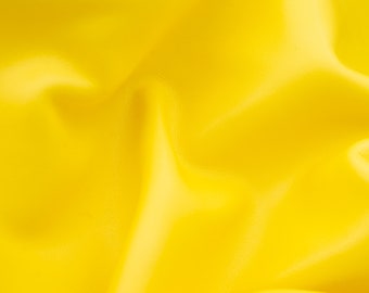 Może przedstawiać: Zbliżenie na jasnożółty materiał o gładkiej, lekko fakturowanej powierzchni. Materiał jest złożony i udrapowany, tworząc miękkie, płynne linie.