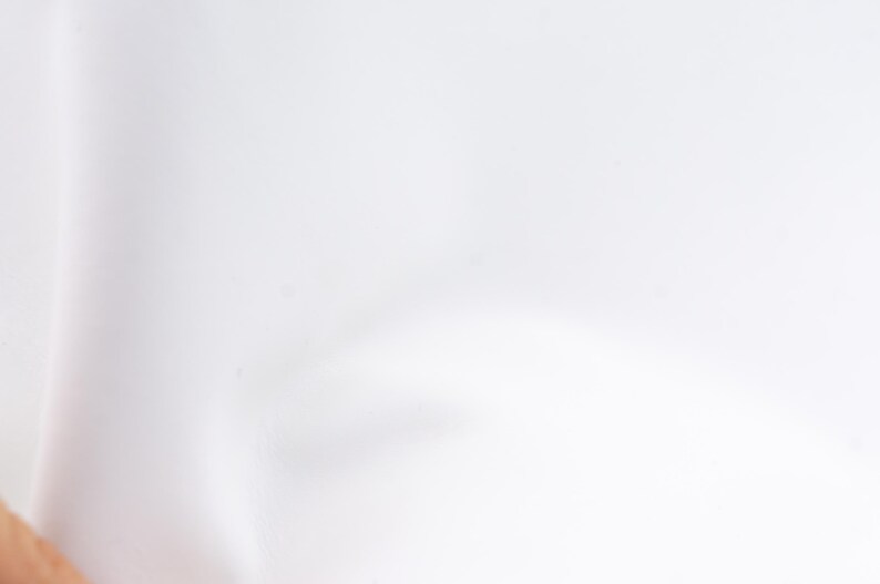 Pode incluir: Um close-up de tecido branco, possivelmente roupa ou t&ecirc;xtil. O material parece liso e limpo, com ligeiras varia&ccedil;&otilde;es na textura e no tom. A ilumina&ccedil;&atilde;o &eacute; suave, criando sombras e destaques suaves.