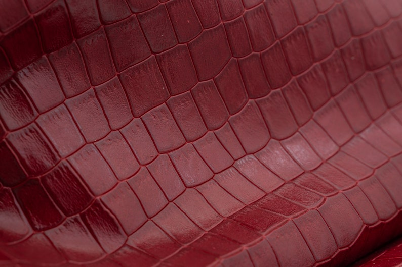 May include: Close-up of a deep red textured leather with a crocodile pattern.