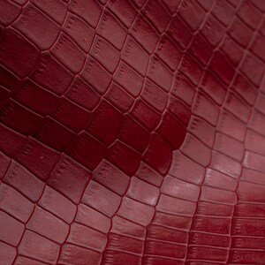 May include: Close-up of a burgundy faux leather material with a crocodile-embossed pattern.