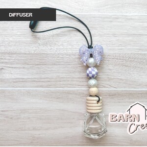 May include: A car air freshener with a bow-shaped top and a string. The air freshener has a clear glass bottle at the bottom and a series of beads in shades of purple, white, and wood. The word "DIFFUSER" is printed on a black rectangle.