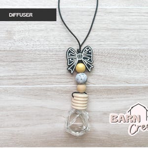 May include: A black and white bow-shaped diffuser charm with a string, yellow, gray, and wooden beads, and a clear glass bottle. The word "DIFFUSER" is in a black rectangle at the top. The Barn Creek Boutique logo is in the bottom right corner.
