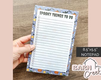 May include: A notepad with a Halloween theme, featuring a list titled "Spooky Things To Do." The notepad has a blue border with ghosts, pumpkins, and bats. The notepad measures 8.5" x 5.5".