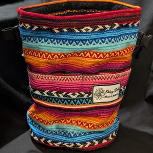 以下が含まれることがあります： 赤、オレンジ、青、黒の幾何学模様が施されたカラフルなクライミングチョークバッグ。バッグには黒い紐の留め具と、「Daisy Chalk Made in Australia」と書かれた小さなラベルが付いています。