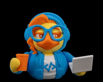 May include: A blue rubber duck wearing headphones and glasses, holding a cup of coffee and a laptop. The duck is wearing a blue hoodie with the code "< >" on the front.