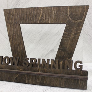 May include: A wooden record stand with a triangular frame and a shelf. The stand has the words "NOW SPINNING" cut out of the wood.