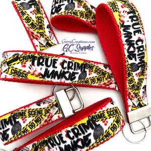 May include: A set of four red and yellow keychains with a white background. The keychains feature a black and white graphic of a crime scene tape with the text "TRUE CRIME JUNKIE".